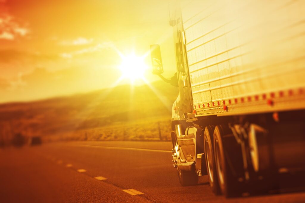 A truck driving on a highway during a bright sunset.